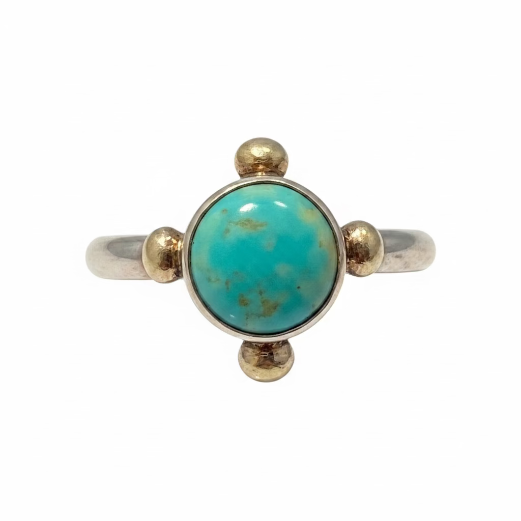 A sterling silver ring featuring a large oval turquoise cabochon stone with four accents forming a cross, against a white background.
