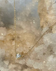 A delicate gold chain necklace with a small heart-shaped clear cubic zarconia gemstone pendant, displayed on a natural crystal geode.