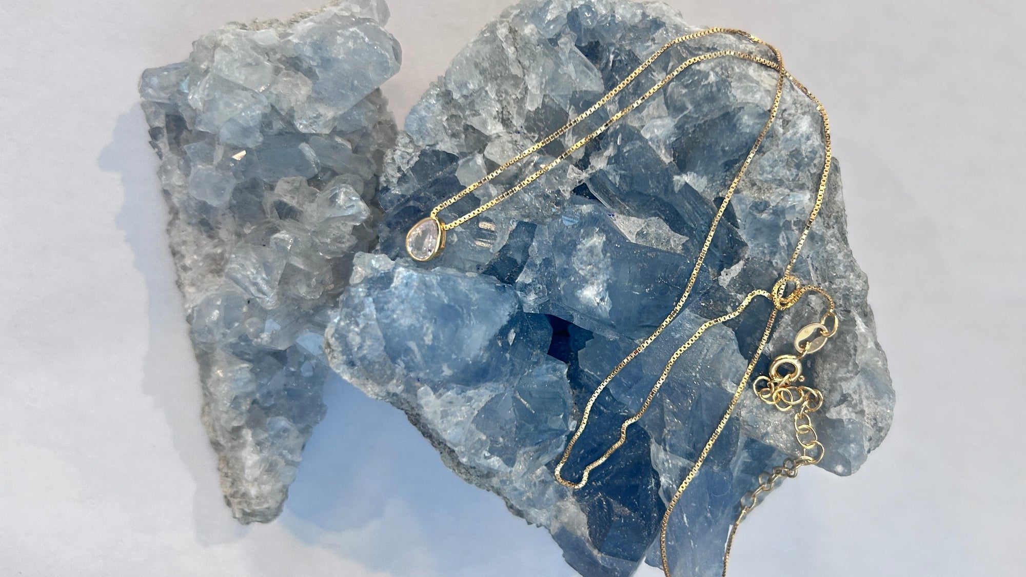 A gold-plated/ gold vermeil teardrop Cubic zarconia clear crystal pendant necklace with a delicate design on a box chain, displayed in front of a crystal.