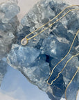 A gold-plated/ gold vermeil teardrop Cubic zarconia clear crystal pendant necklace with a delicate design on a box chain, displayed in front of a crystal.