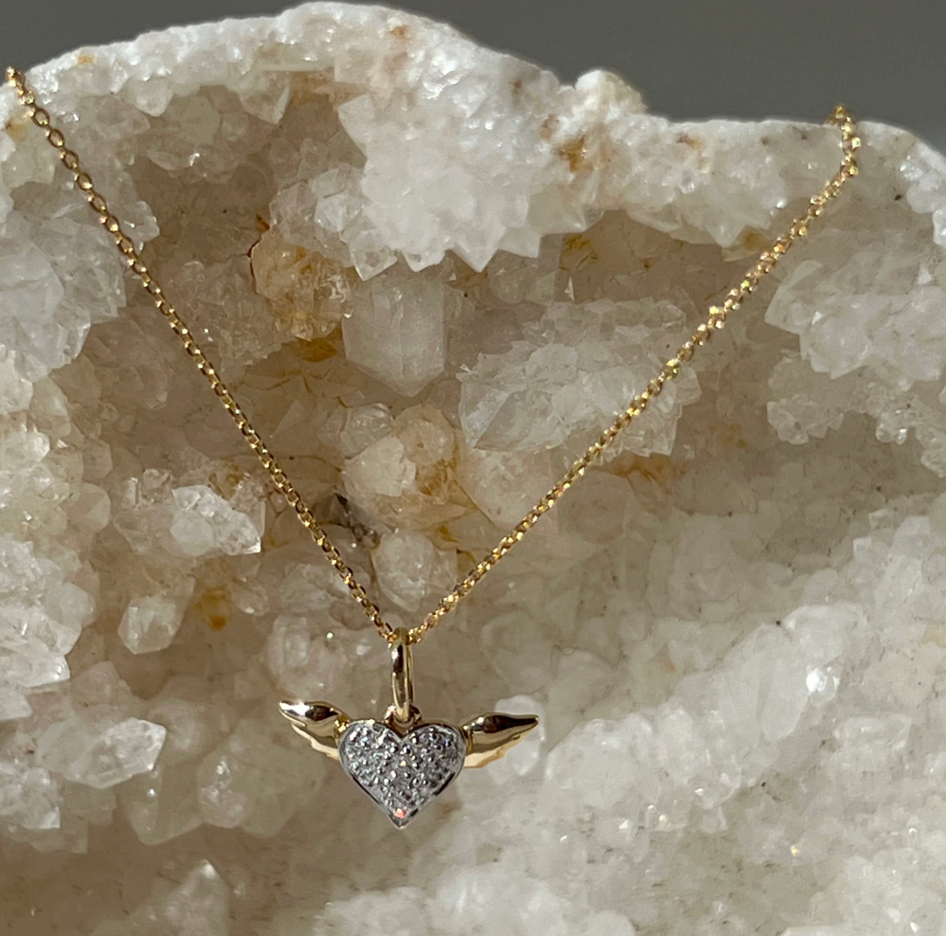 14k gold necklace with a winged heart-shaped pendant  with pave diamonds on a 16 inch cable chain with a crystal background.