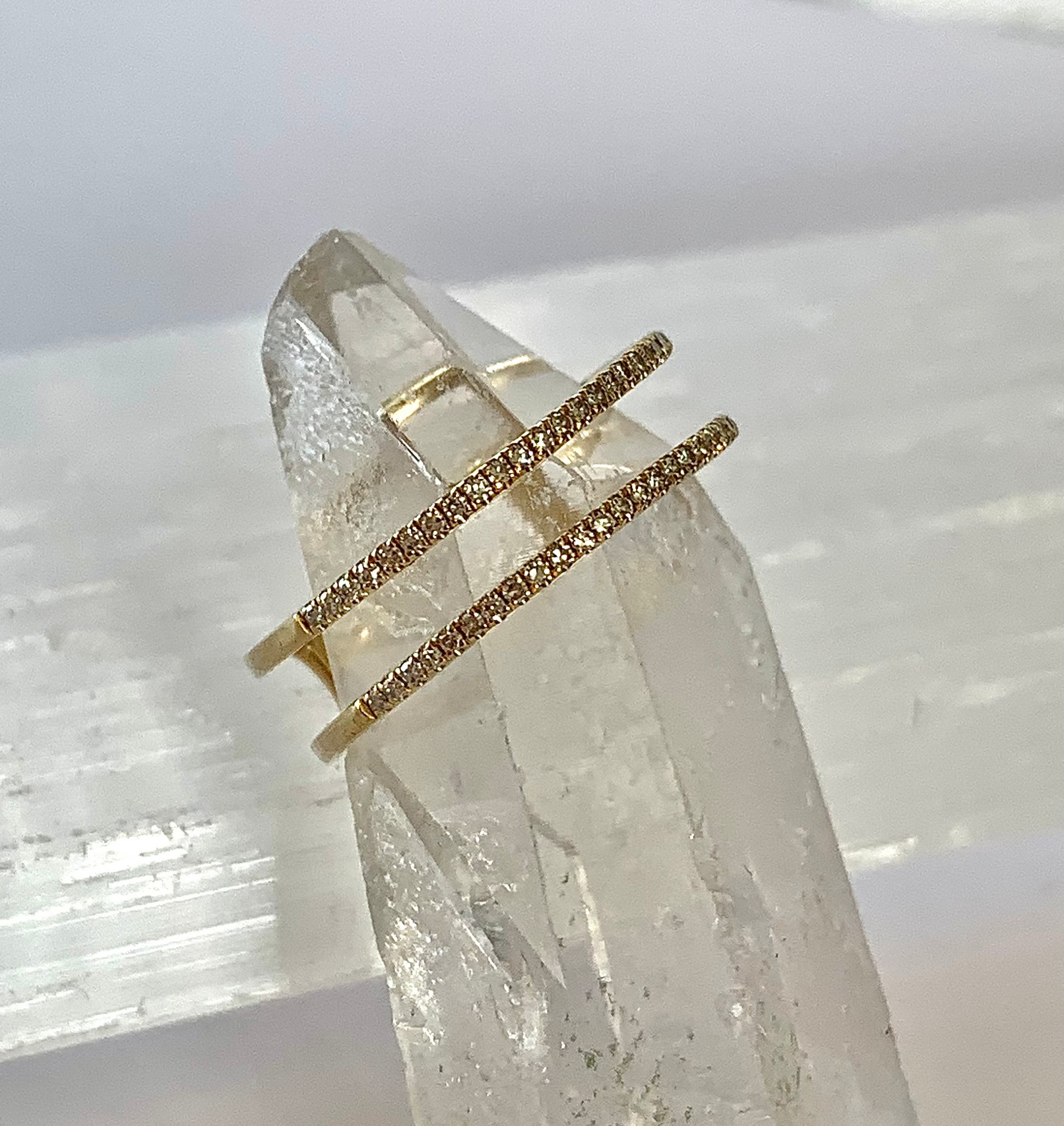 A solid 14k gold double band ring with diamonds along both bands, displayed on a clear crystal.