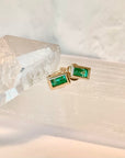A pair of 14k yellow gold emerald stud earrings on a crystal surface.