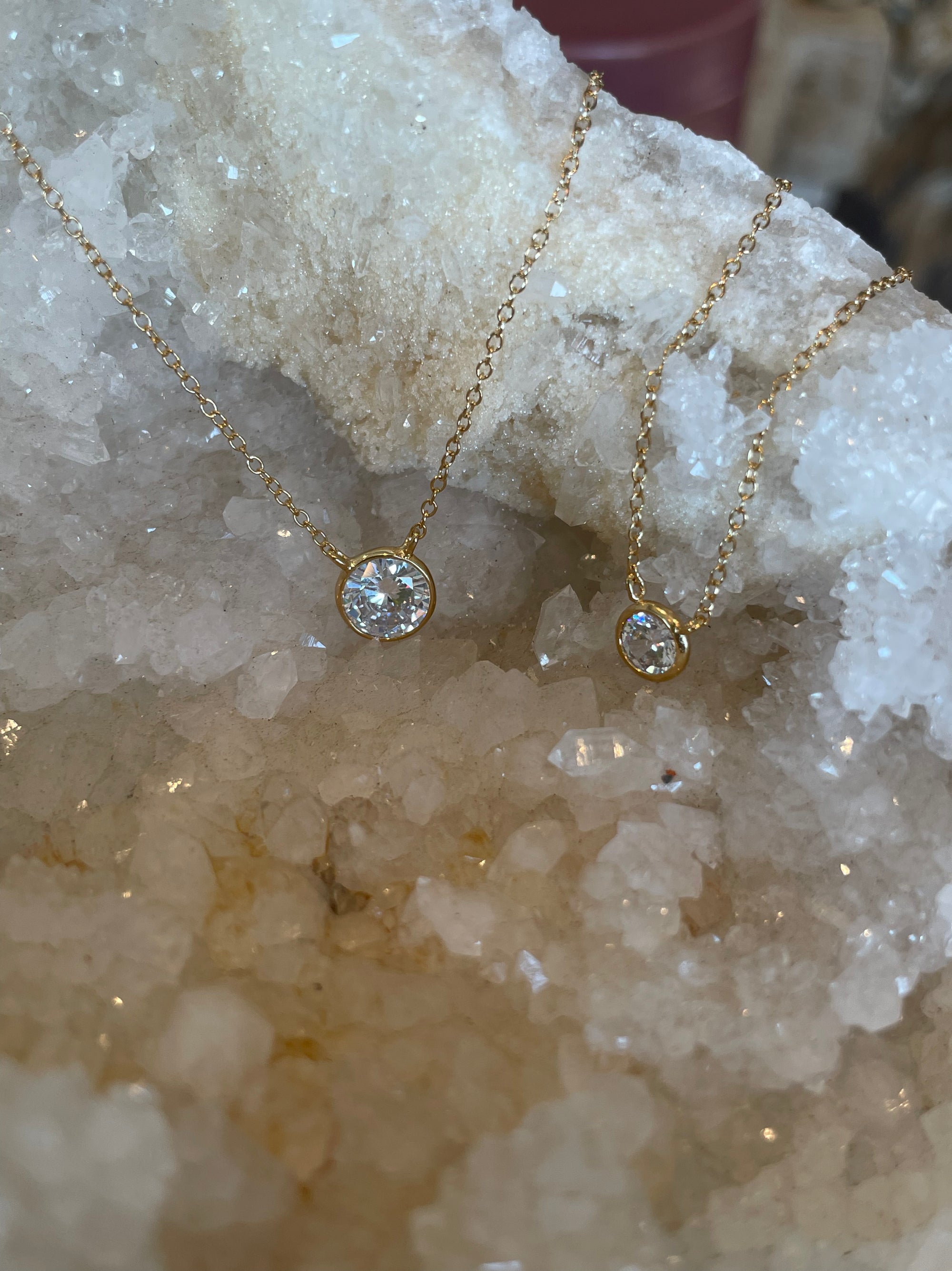 A dainty cubic zarconia bezel necklace with a gold double plated sterling silver chain, displayed against a crystal background.