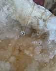 A dainty cubic zarconia bezel necklace with a gold double plated sterling silver chain, displayed against a crystal background.