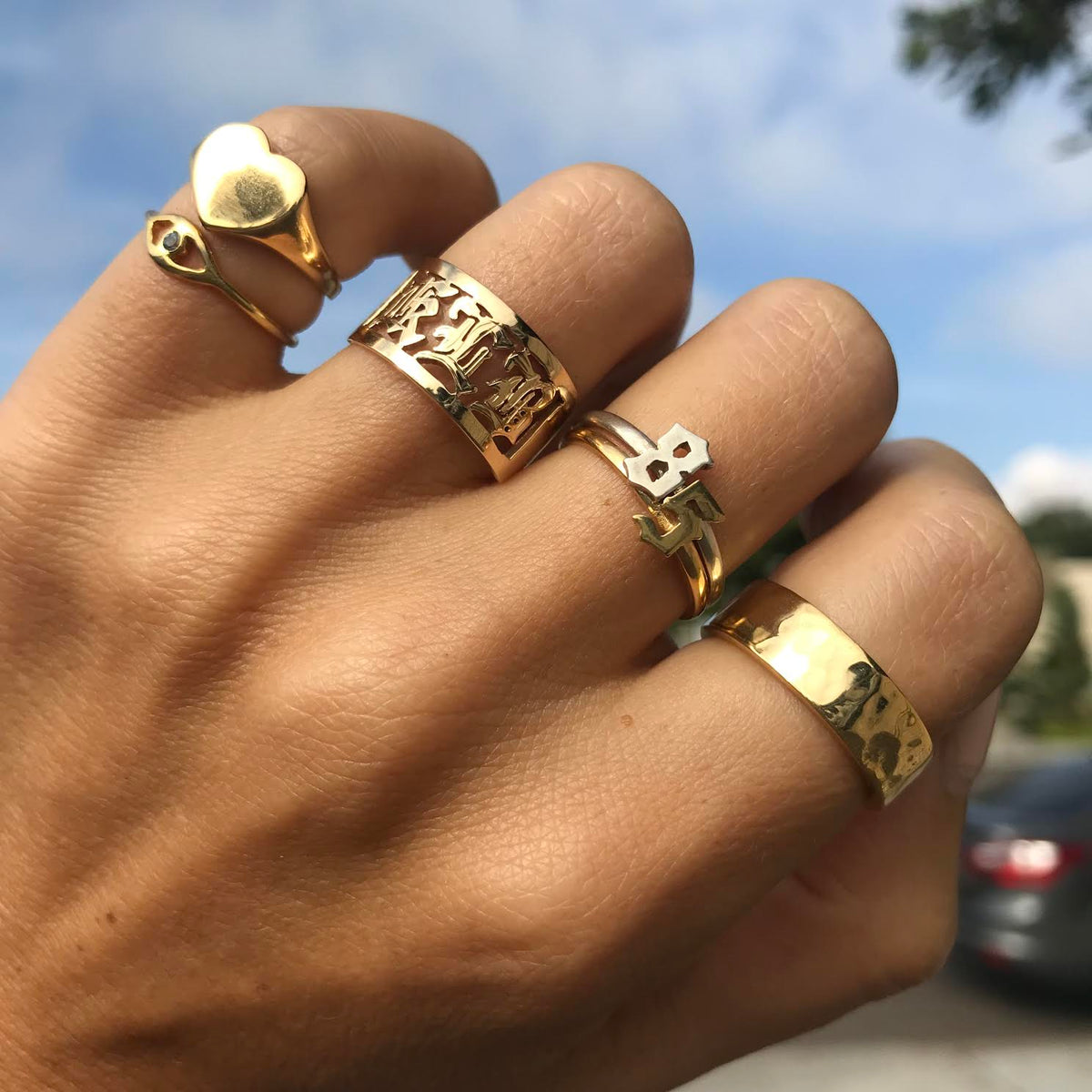 A hand with many different Jacqueline Nicole Brown rings, the pointer finger features a hammered cigar band. 