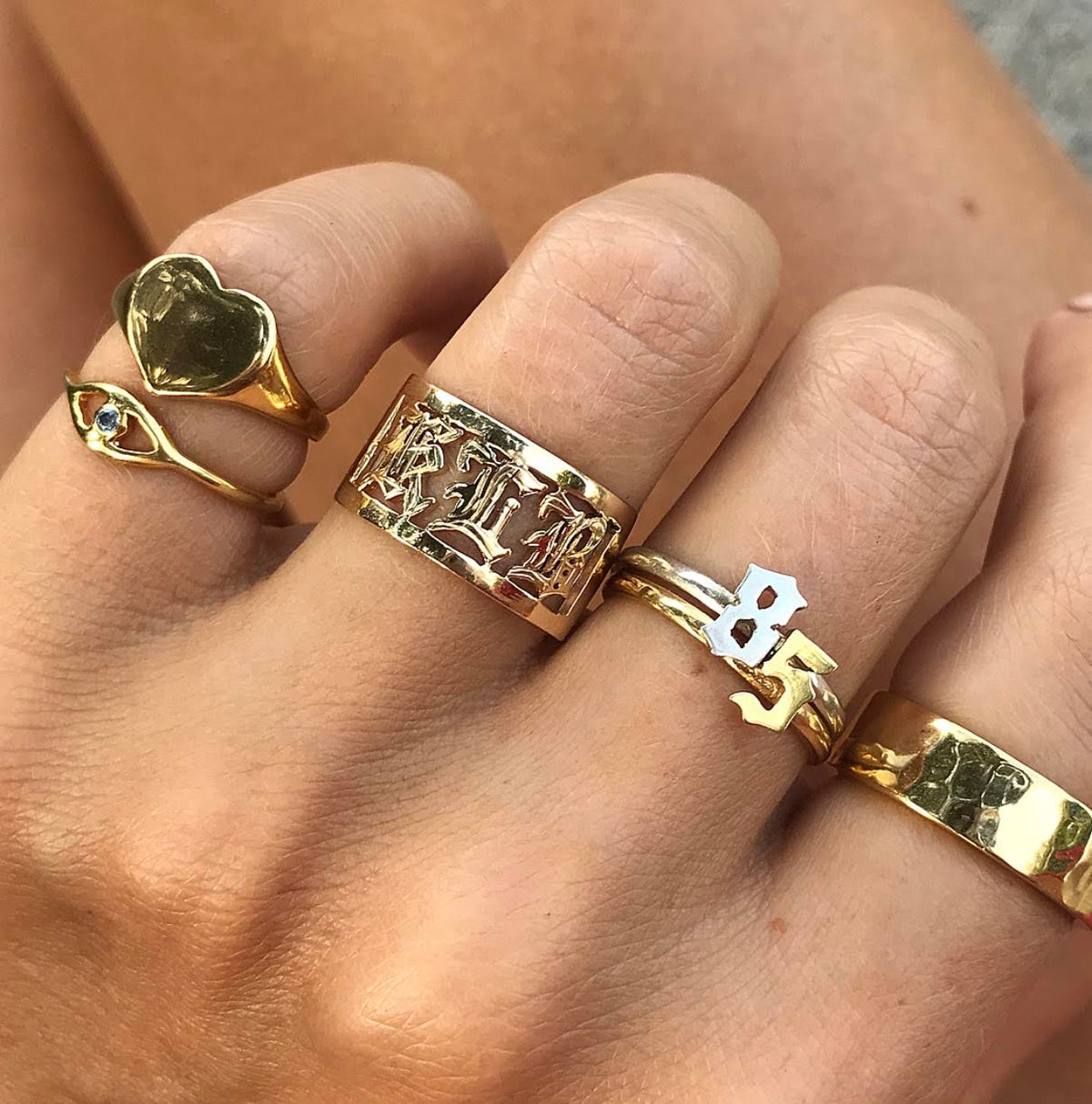 A hand showcasing many different JNB Style gold vermeil rings, with a hammered band on the pointer finger. 