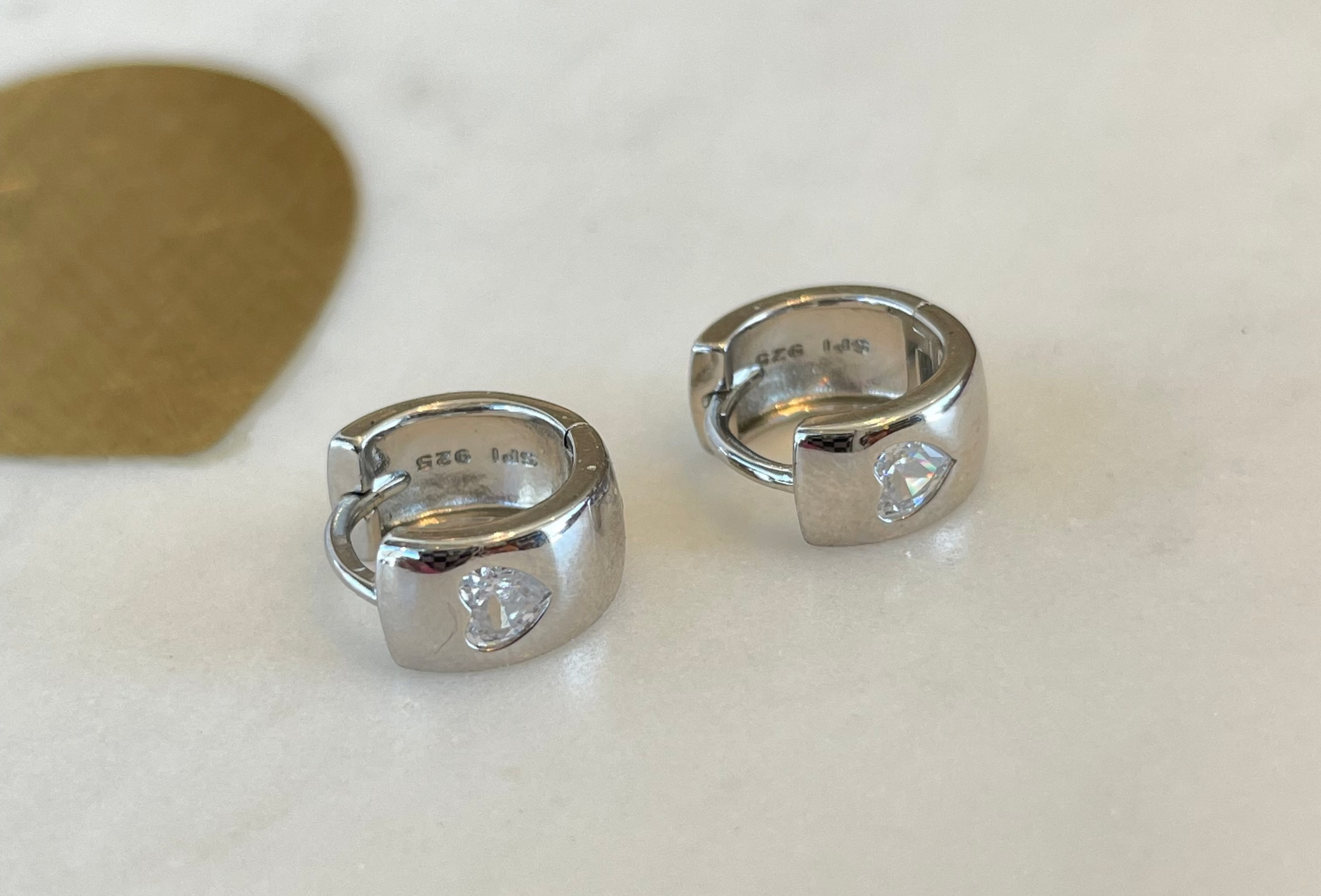 A pair of silver earrings with a heart-shaped design made from Cubic Zarconia Crystal this hypo-allergenic earring is displayed quartz plate.